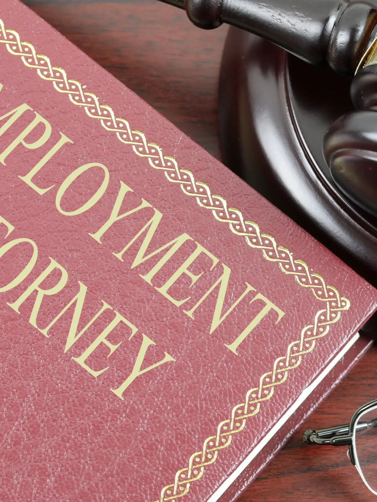 A red "Employment Attorney" legal book beside a wooden judge's gavel and reading glasses on a wooden surface — illustrating attorney fees and legal representation for employment law cases in Texas.